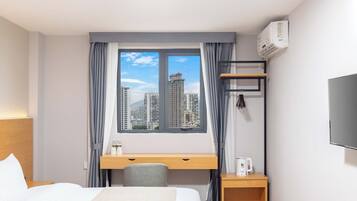 Habitació d'hotel amb llit, escriptori, cadira, televisió i finestra amb vista a la ciutat.