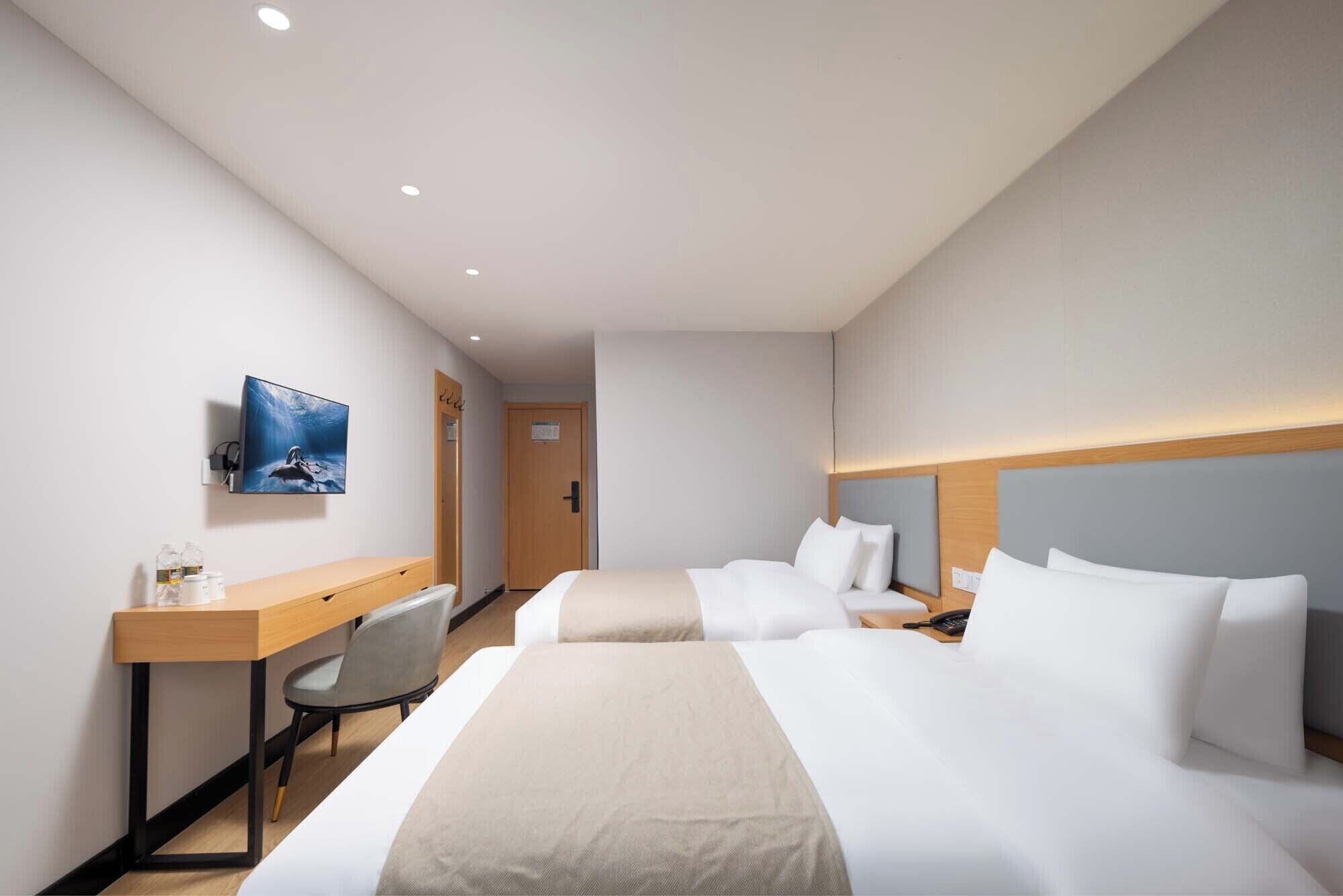 A hotel room with two beds, a desk, a chair, a television, and a door.
