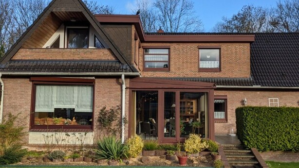 Une maison à deux étages, avec une façade en briques, de grandes fenêtres et un porche à l’avant.