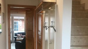 A hallway with a wooden ceiling, a tiled floor, a staircase to the right, and a door leading to a room with a black chair and a table. - Vacation home Hasi by Interhome (Friederikensiel)