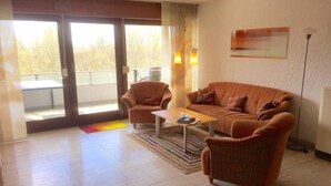 Una sala de estar con un sofá, dos sillones, una mesa de centro y un ventanal corredizo que da a un espacio al aire libre.
