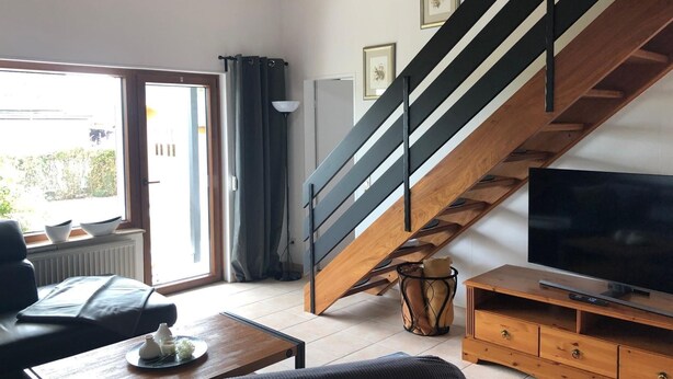 Uma sala de estar moderna com escada de madeira, televisão e área de jantar com mesa e cadeiras.