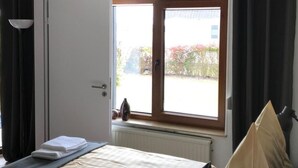 Quarto com cama, janela com cortinas, radiador e luminária no teto.
