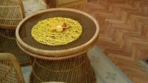 Una stanza con mobili in vimini, un letto, un tavolino con un sottobicchiere e una pianta in vaso.