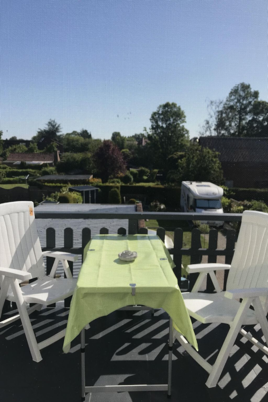 An outdoor seating area with a table and chairs, surrounded by greenery and a fence.