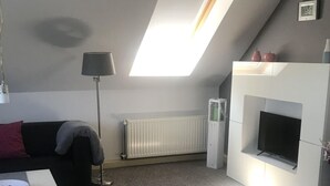 Un salon moderne doté d’un plafond en pente, d’une cheminée intégrée, d’un téléviseur à écran plat et d’un canapé.