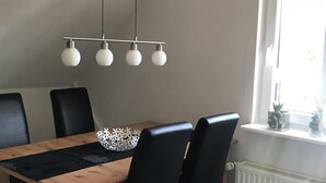 Un espace repas avec une table en bois, des chaises noires et un luminaire suspendu.