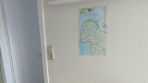 Una habitación con una mesa de madera y dos sillas plegables, un mapa en la pared y suelo de baldosas.