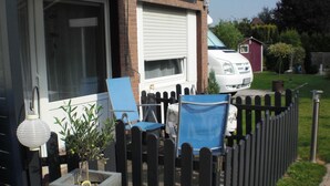 Una propiedad residencial con un patio cercado, un coche blanco aparcado en la entrada y un pequeño jardín con una planta en maceta.