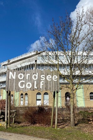 Une enseigne indiquant « Nordsee Golf » devant un bâtiment doté de nombreuses fenêtres, avec un ciel bleu dégagé.
