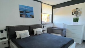A modern bedroom with a large bed, bedside tables, a desk, and a window with blinds. - Freistehendes Ferienhaus in Tossens mit Terrasse by Interhome (Burhave)