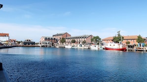 En hamn vid vattnet med förtöjda båtar, en stor byggnad med flera våningar och en klarblå himmel.