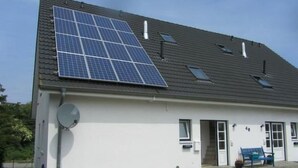 En byggnad med ett sluttande tak, solpaneler, en satellantenn och en liten utomhusplats med sittmöbler.