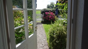 A garden view from a doorway with a gravel path leading to a white fence and a blue umbrella. - Geltinger Birk by Interhome (Gelting)