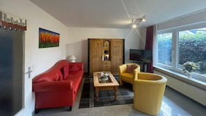 Una sala de estar con un sofá rojo, un sillón amarillo, un aparador de madera y un televisor.