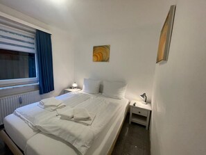 Een hotelkamer met een tweepersoonsbed, een nachtkastje met een lamp, een raam met blauwe gordijnen en een schilderij aan de muur.