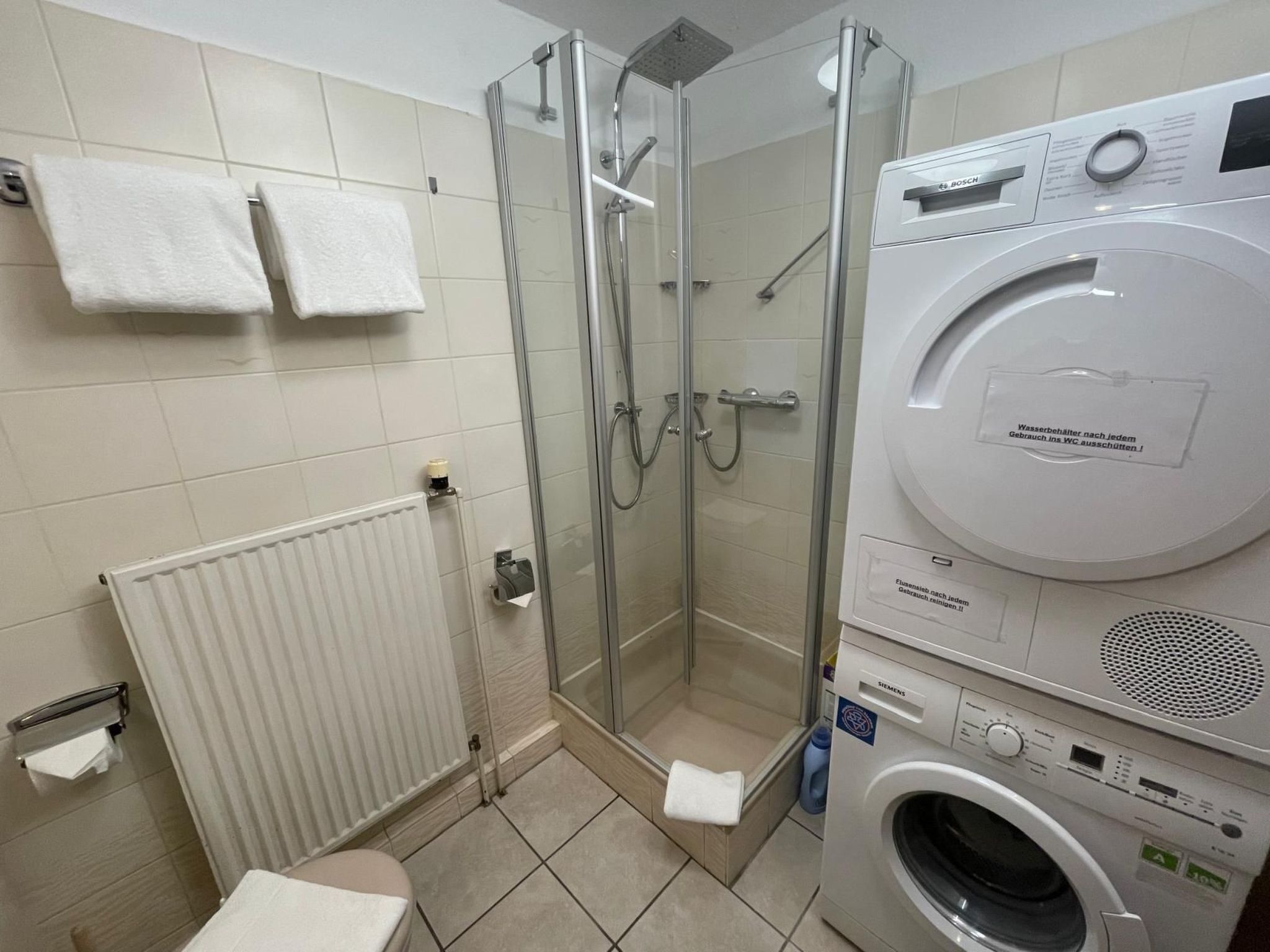 Kylpyhuoneessa on lasiseinällä varustettu suihku, wc, patteri sekä päällekkäin sijoitettu pesukone ja kuivausrumpu.