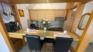 Une cuisine compacte avec des meubles en bois, une table à manger avec quatre chaises, une machine à café et un four à micro-ondes.