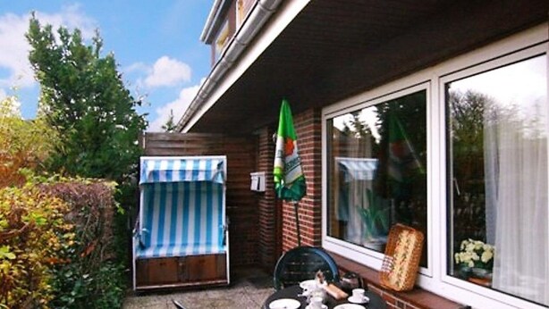 Un espace patio avec une table dressée pour deux personnes, une chaise à rayures bleues et blanches et un parasol vert.