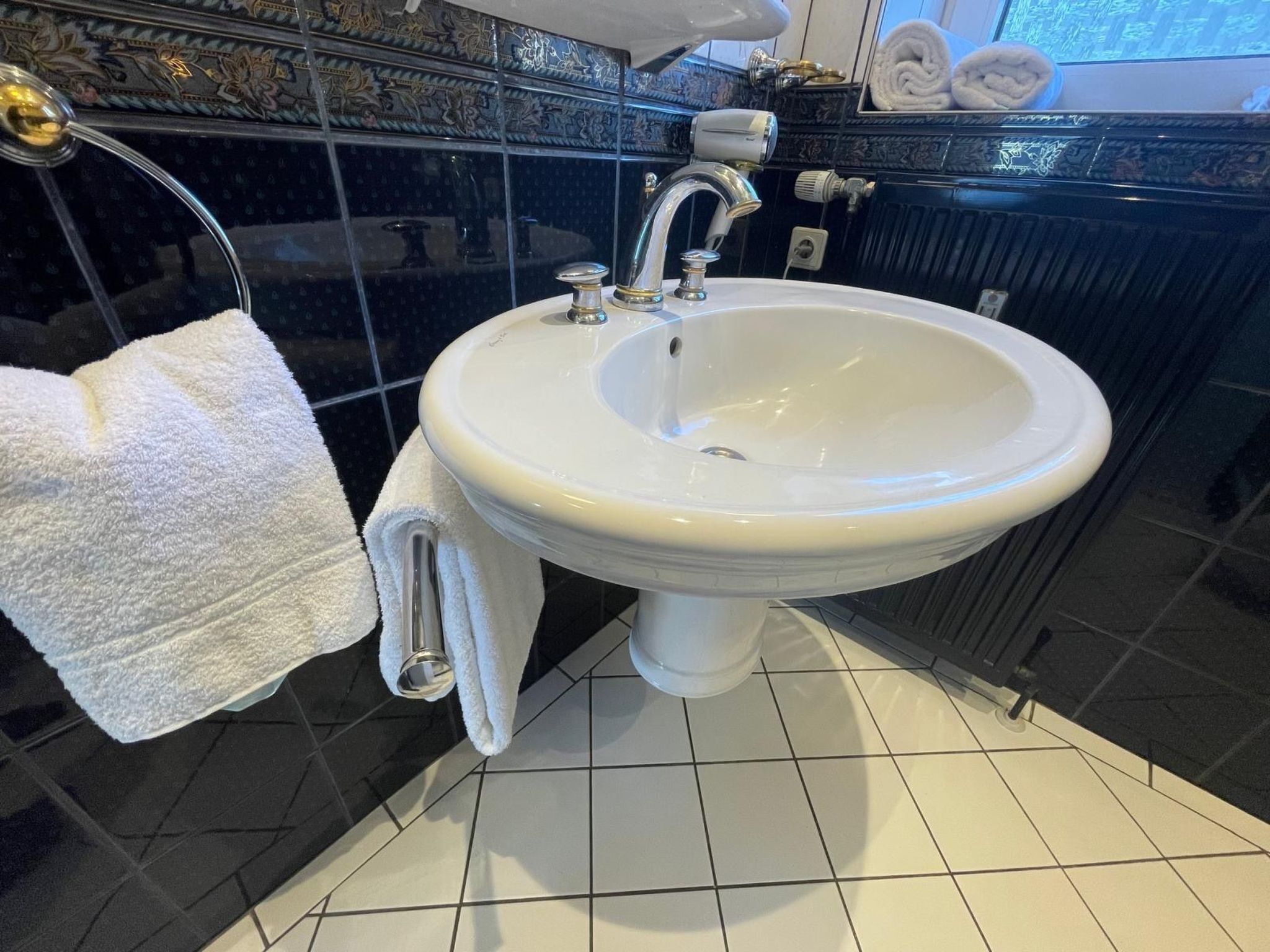 Un baño con un lavamanos blanco, paredes de azulejos negros y una toalla blanca en el suelo.