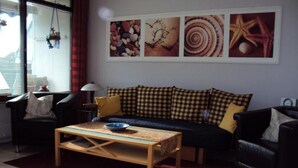 A living room with a sofa, armchairs, a coffee table, and a red rug. There are framed pictures on the wall. - Pratzat by Interhome (Büsum)