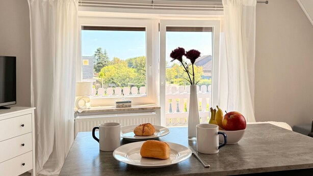 Ein Essbereich mit einem für das Frühstück gedeckten Tisch, einem Fernseher und Blick ins Freie.