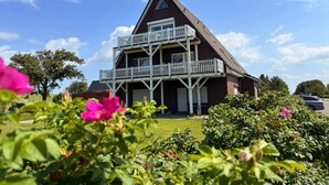 Ein zweigeschossiges Haus mit Balkon, umgeben von üppigem Grün und blühenden Pflanzen.