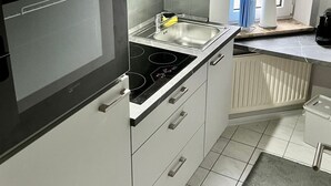 A modern kitchen with white cabinets, a stainless steel sink, and a built-in oven. - Nordseeperle by Interhome (Cuxhaven)