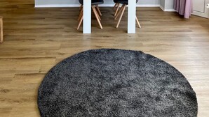 A dining area with a white table and four chairs, a painting of a landscape on the wall, a round rug on the floor, and a door in the background. - Nordseeperle by Interhome (Cuxhaven)