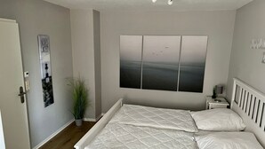 A bedroom with a bed, a nightstand, a wall-mounted artwork, and a door. - Nordseeperle by Interhome (Cuxhaven)