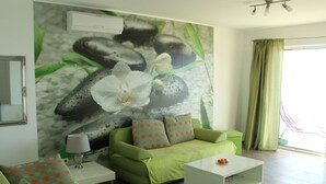 A living room with green sofas, a white coffee table, and a large floral mural on the wall. - Gemütliche Ferienwohnung in Mlini mit Großer Terrasse by Interhome (Dubrovnik/Mlini)