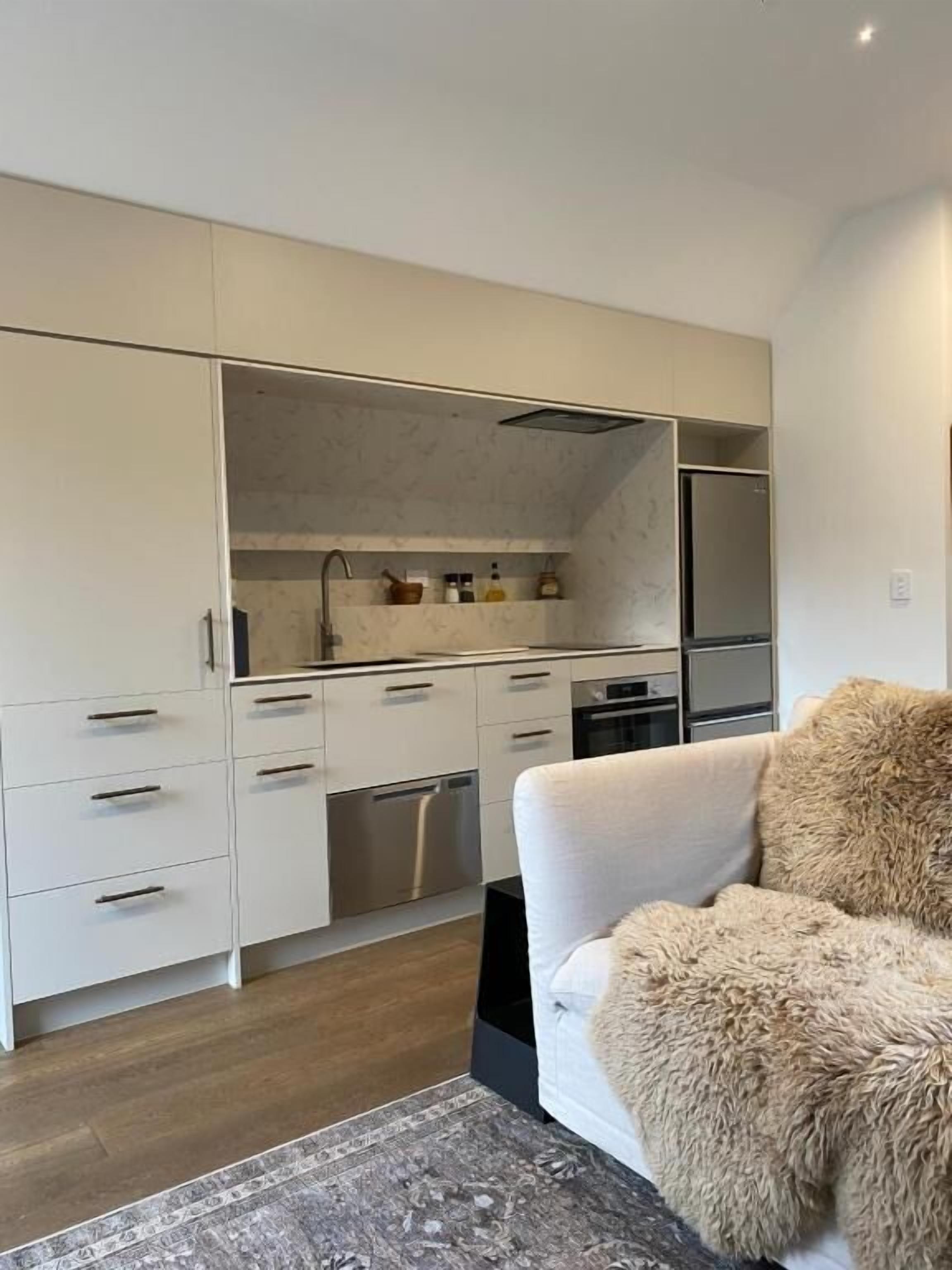 A modern kitchen with white cabinets, a built-in oven, and a refrigerator.