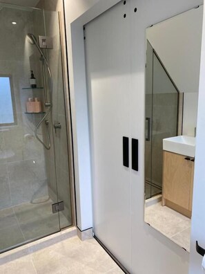 Une salle de bain moderne avec une douche à l’italienne en verre, un grand miroir et un meuble-lavabo blanc.