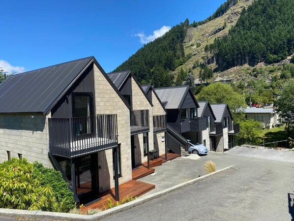 Une rangée de bâtiments modernes à deux étages, dotés de balcons, se dressant sur un fond de paysage montagneux.
