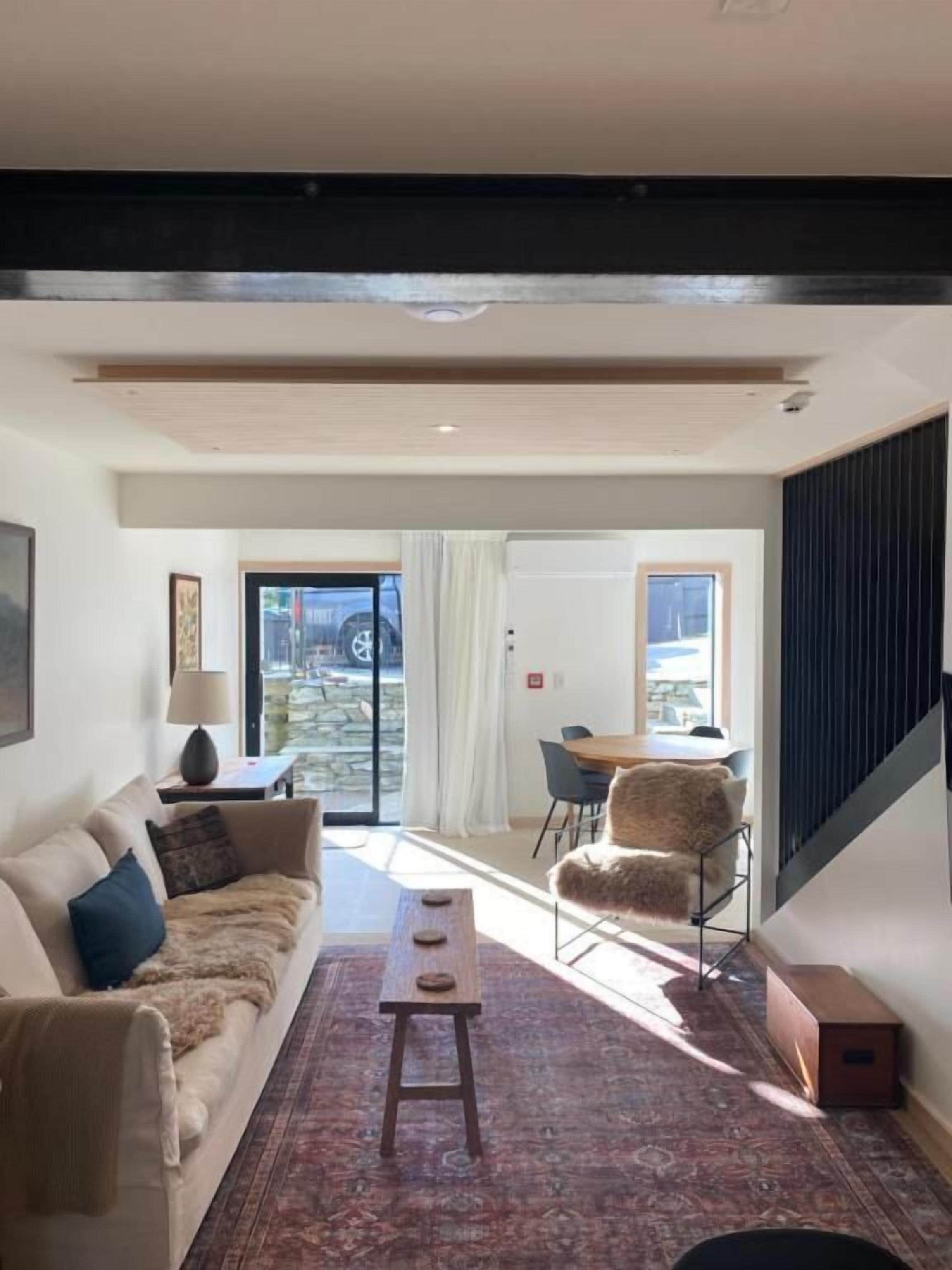 Una sala de estar moderna con un sofá, una mesa de centro, un tapete estampado y un área de comedor con una silla y una mesa.
