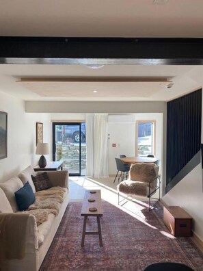 Un salon moderne comprenant un canapé, une table basse, un tapis à motifs et un coin repas avec une chaise et une table.