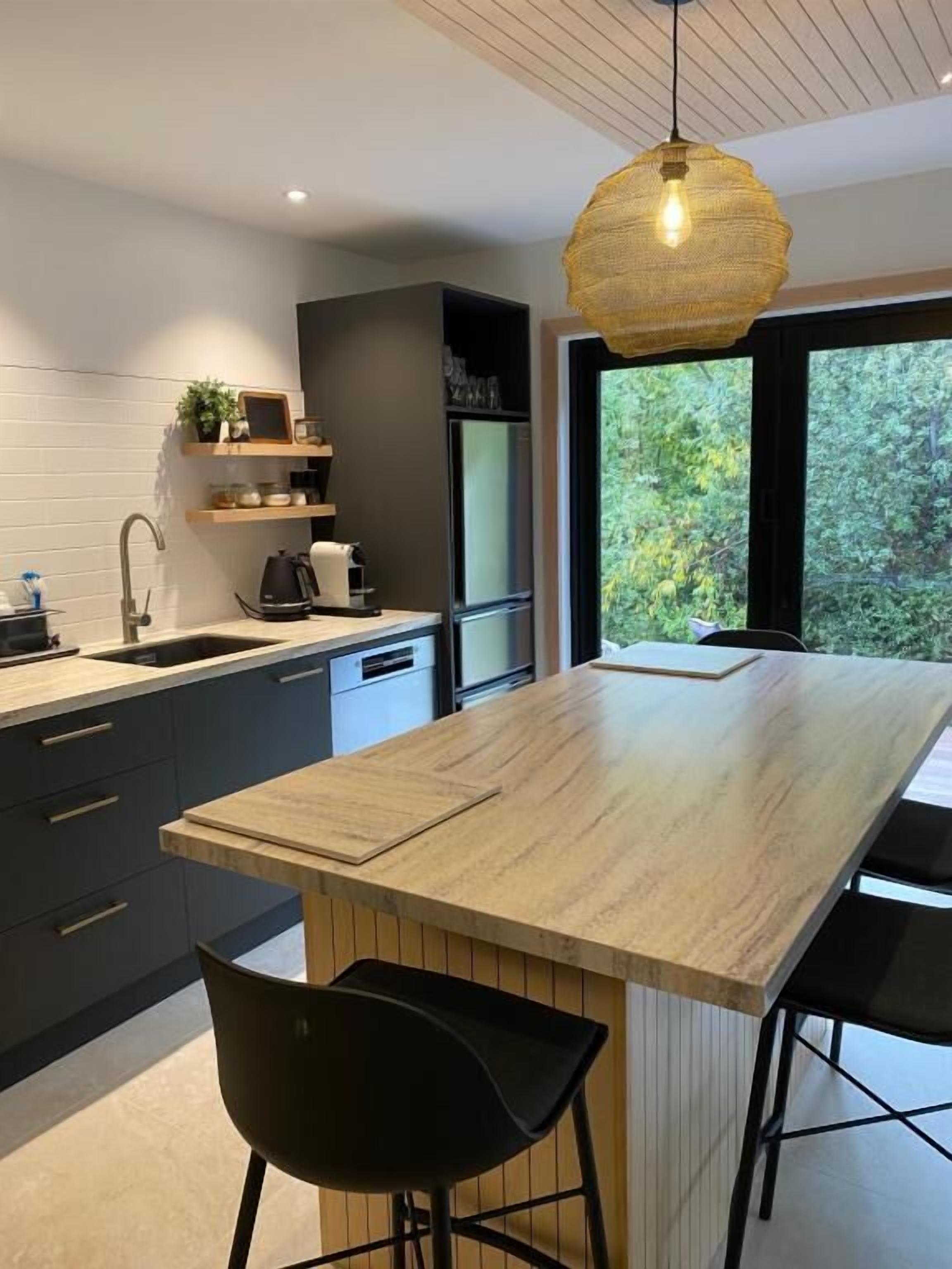 Una cocina moderna con una isla central, armarios oscuros y una lámpara colgante.