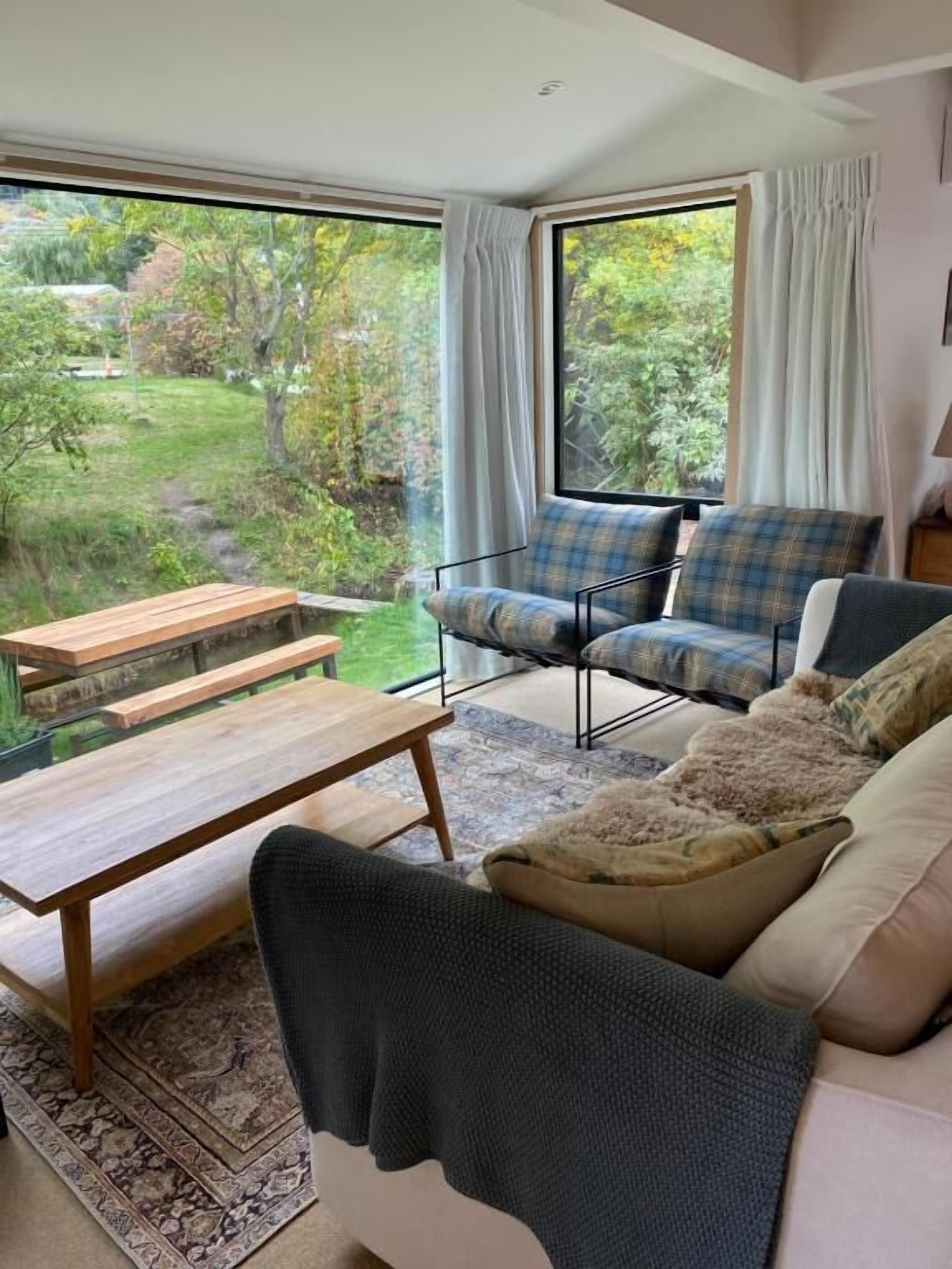 Una habitación con sofá, banca y vistas a un jardín a través de amplios ventanales.