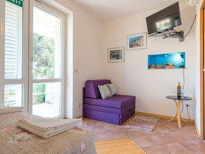 Ein Zimmer mit einem violetten Sofa, einem an der Wand montierten Fernseher und einem kleinen Tisch mit einer Flasche und Gläsern.