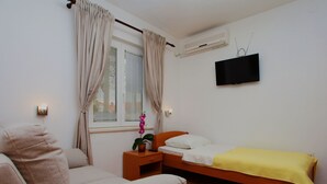 Une chambre avec un lit, un canapé, une table de chevet avec une plante, un téléviseur fixé au mur et un climatiseur.