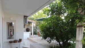 Un espace extérieur abrité, avec des marches menant à une structure blanche, entourée de verdure et de plantes en pot.