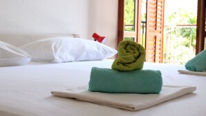 Ein ordentlich bezogenes Bett mit weißen Laken, einem grünen Handtuch und einem zusammengerollten Handtuch auf einem weißen Kissen.