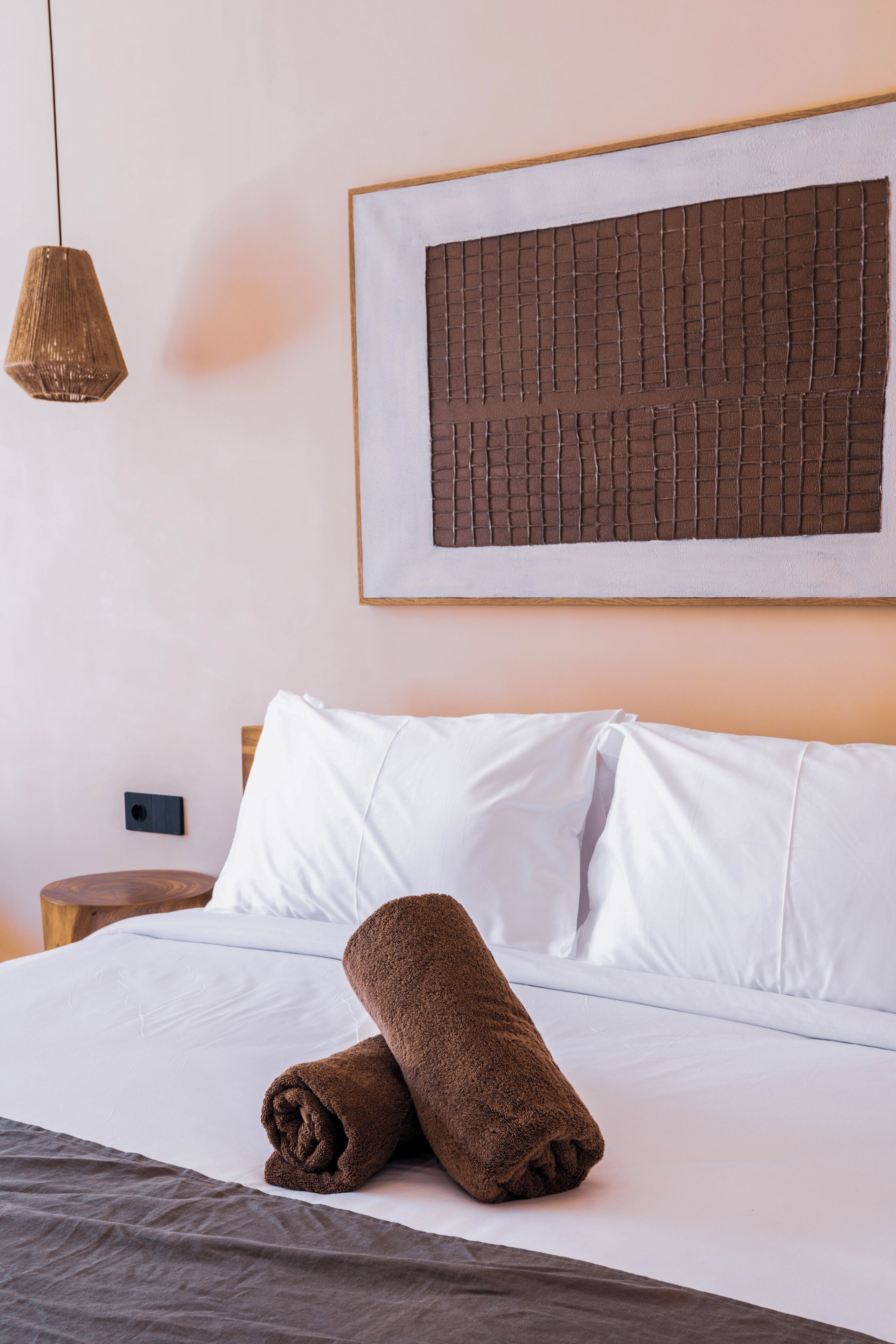 Una cama bien hecha con sábanas blancas, una toalla marrón y una obra de arte abstracta enmarcada en la pared.