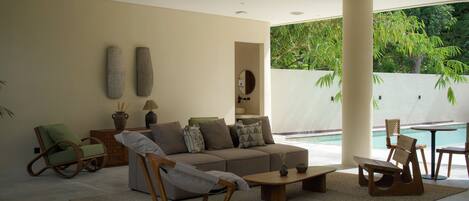 Un salon moderne avec un canapé, des fauteuils, une table basse et une vue sur une piscine.
