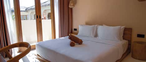 A hotel room with a bed, a chair, a wooden side table, and a view through a sliding door.