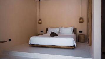 A minimalist bedroom with a bed, two pendant lights, and a small stool.