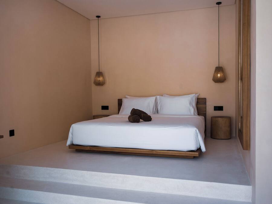 A minimalist bedroom with a bed, two pendant lights, and a small stool.