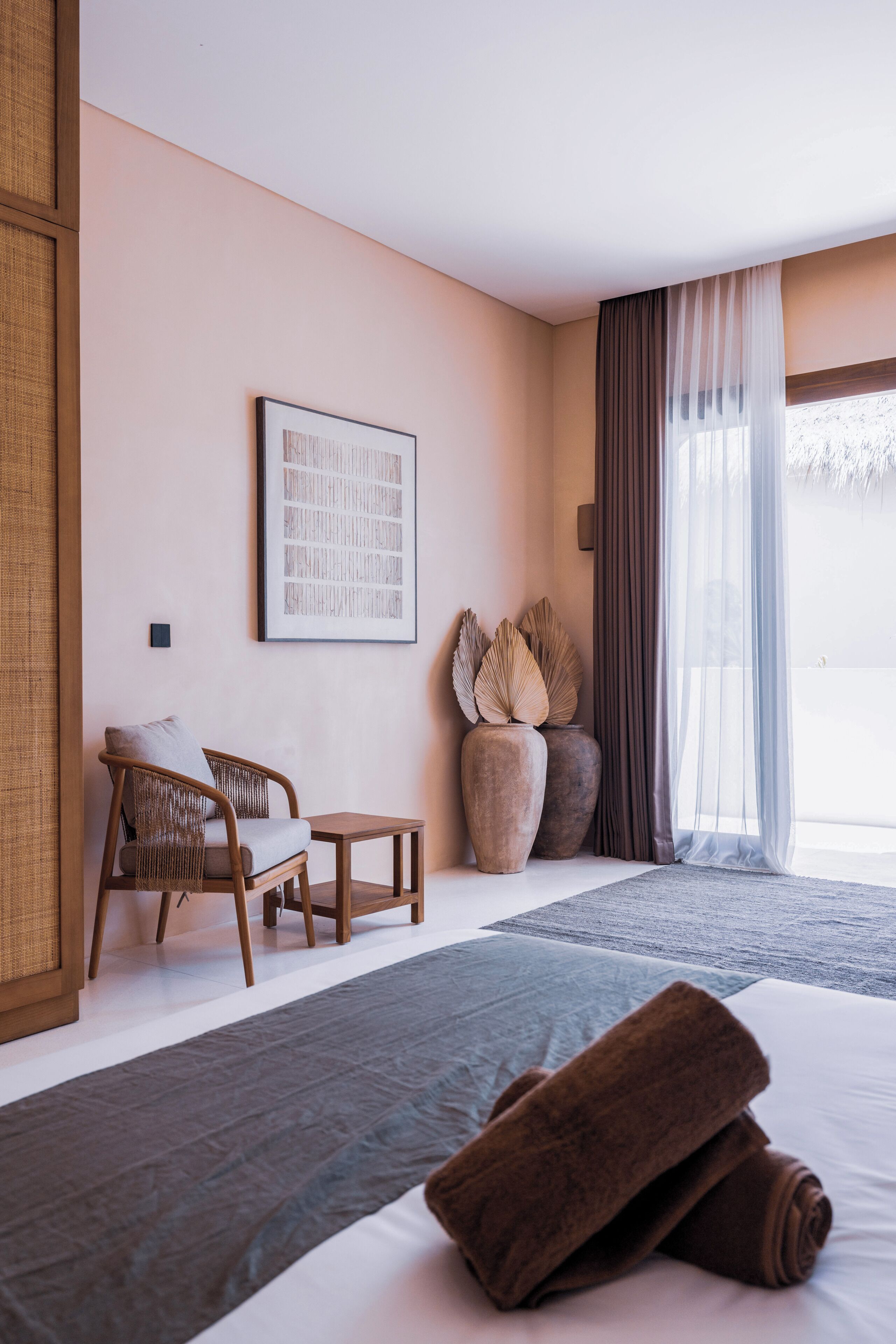 Camera d'albergo con un letto, due poltrone, un tavolino, un quadro incorniciato e un'ampia finestra con tende.