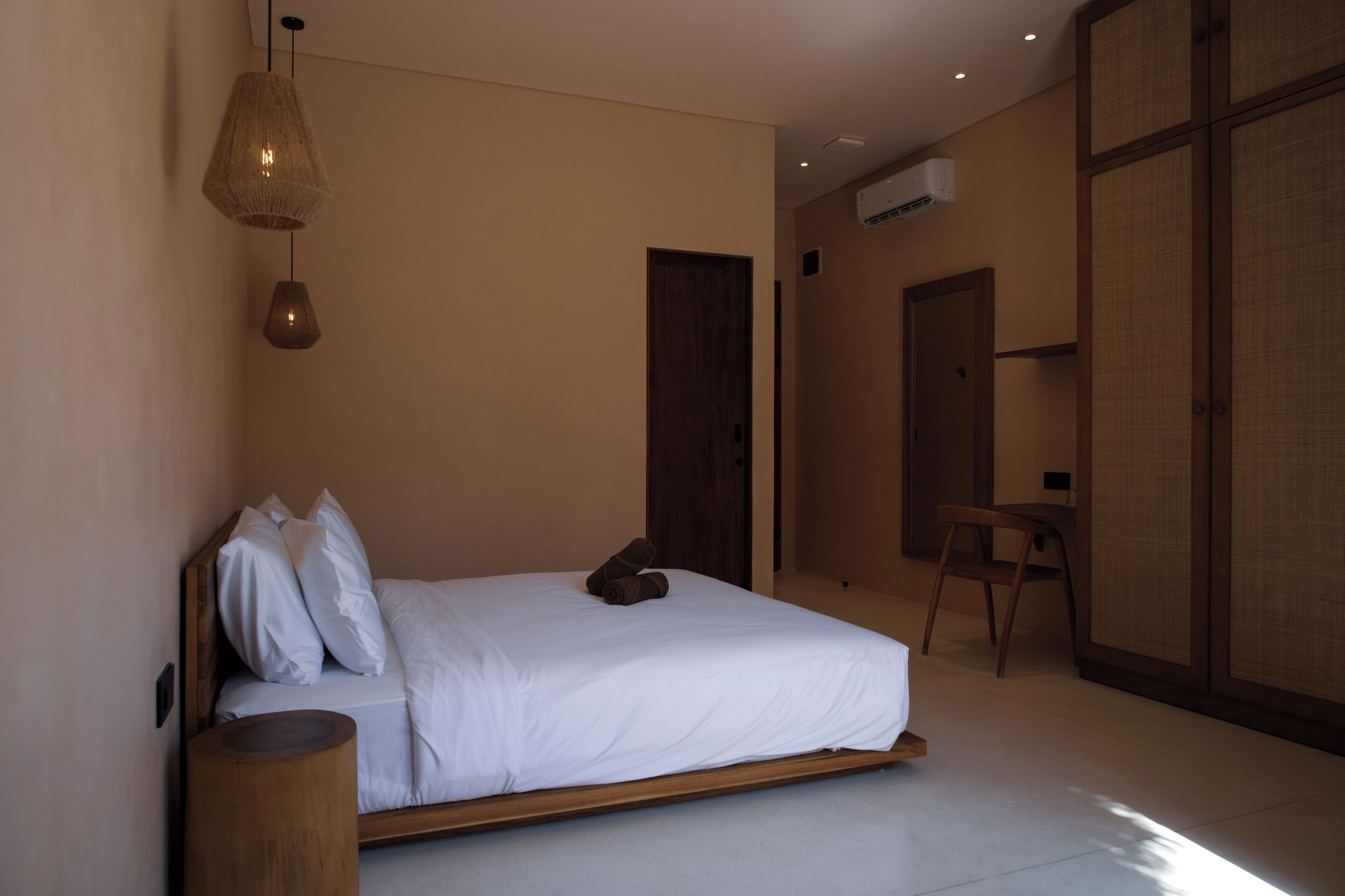 A bedroom with a bed, pillows, a hanging light fixture, a wooden stool, and a sliding door.