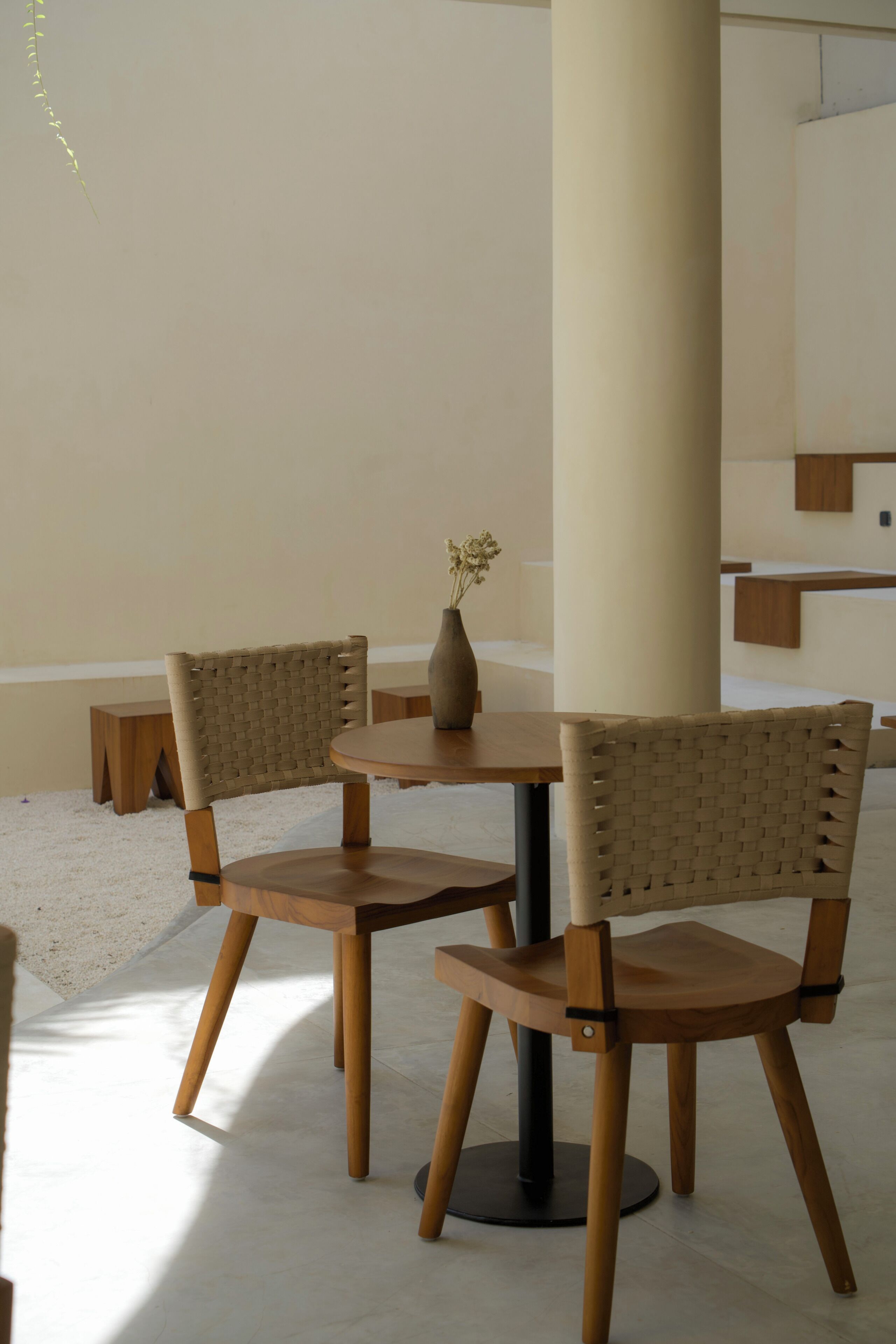 A modern interior with two wooden chairs, a round table, and a vase with flowers.